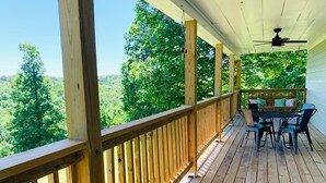 A wooden deck with a table and chairs, overlooking a forested area.