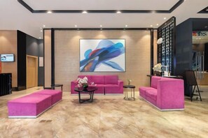 Un vestíbulo con un sofá rosa, una mesa de centro y un cuadro abstracto grande en la pared.
