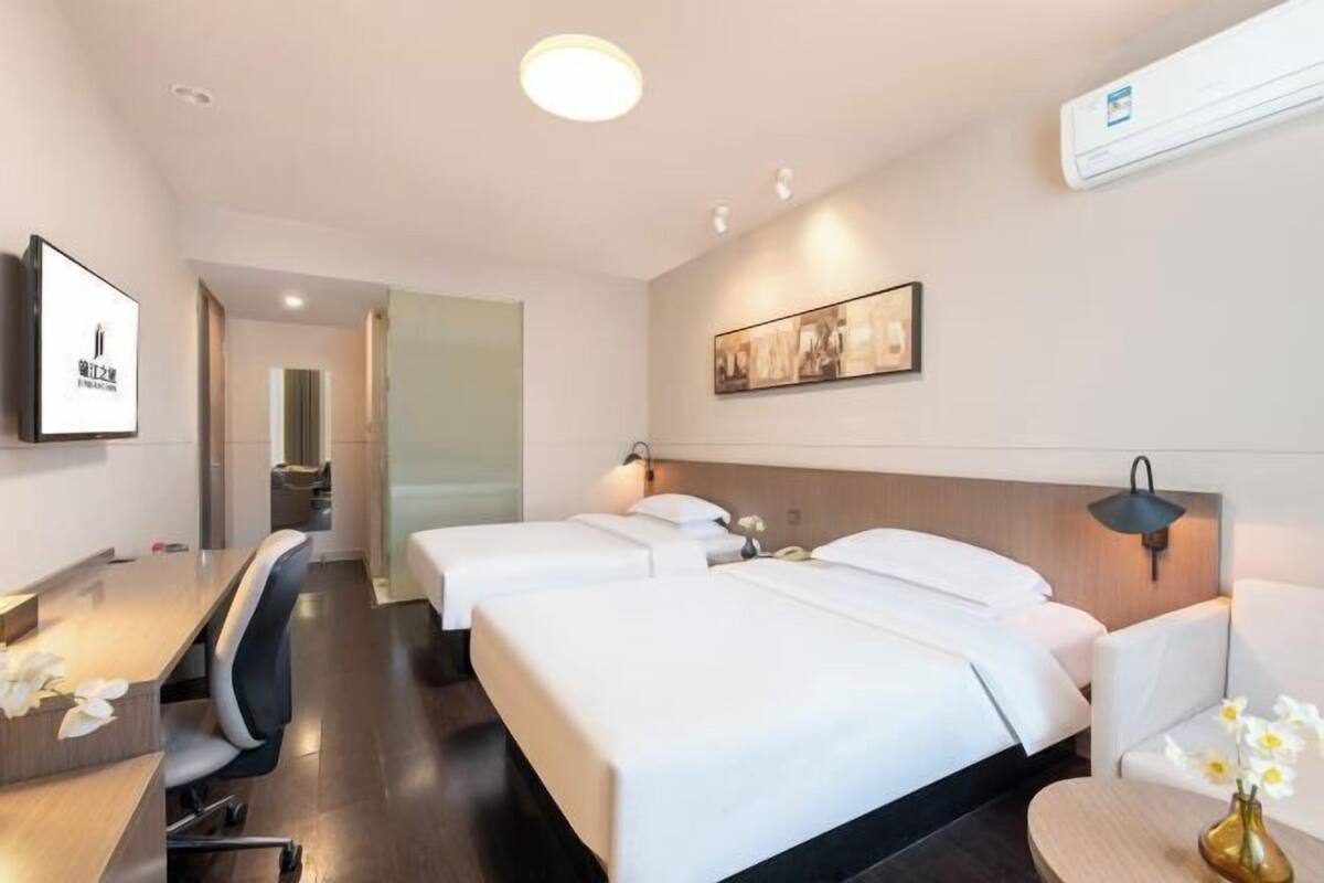 Habitación de hotel con dos camas, un escritorio, una silla, un televisor y aire acondicionado instalado en la pared.
