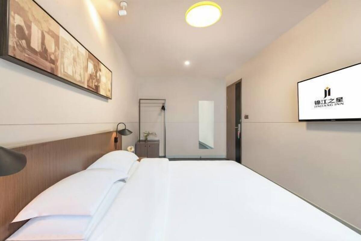 Una habitación de hotel con una cama bien tendida, un televisor montado en la pared y un cuadro enmarcado sobre la cama.