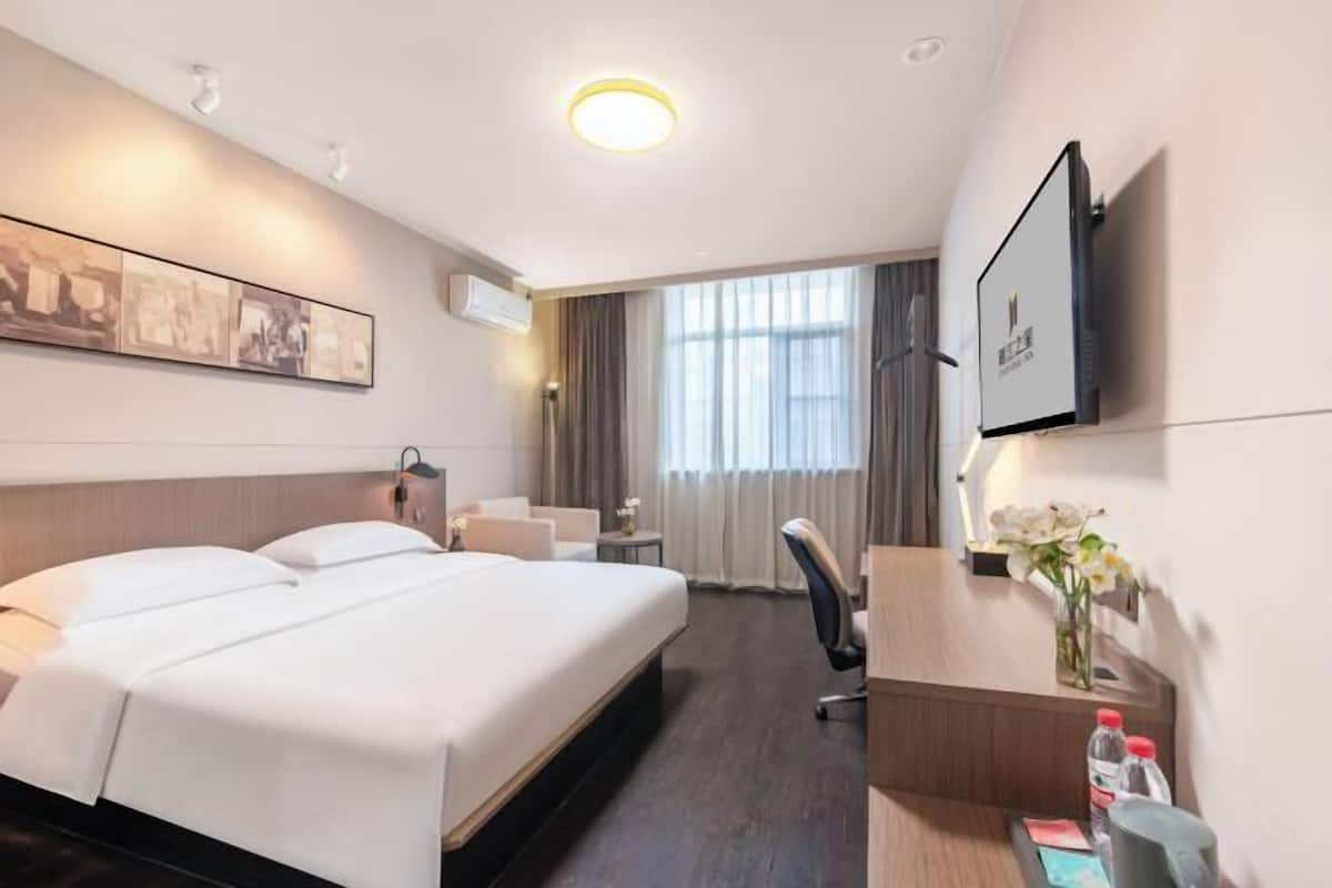 Habitación de hotel con una cama grande, un escritorio, una silla, un televisor y una ventana con cortinas.