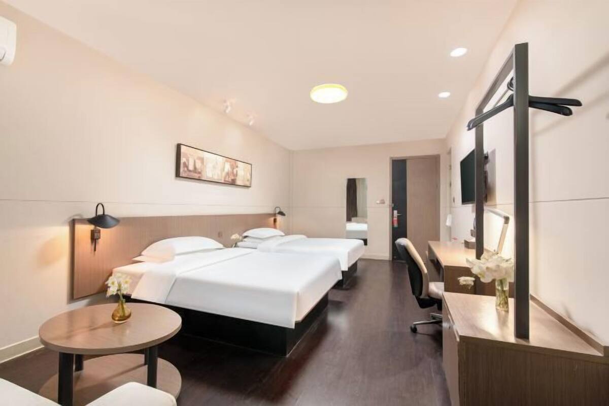 Habitación de hotel con dos camas, un escritorio, una silla, una mesa redonda y un televisor montado en la pared.