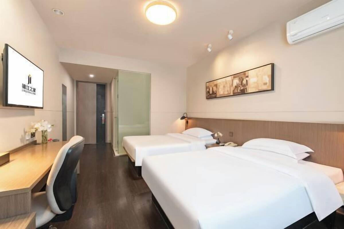 Habitación de hotel con dos camas, un escritorio y una silla. Hay un cuadro en la pared y un equipo de aire acondicionado sobre la cama.