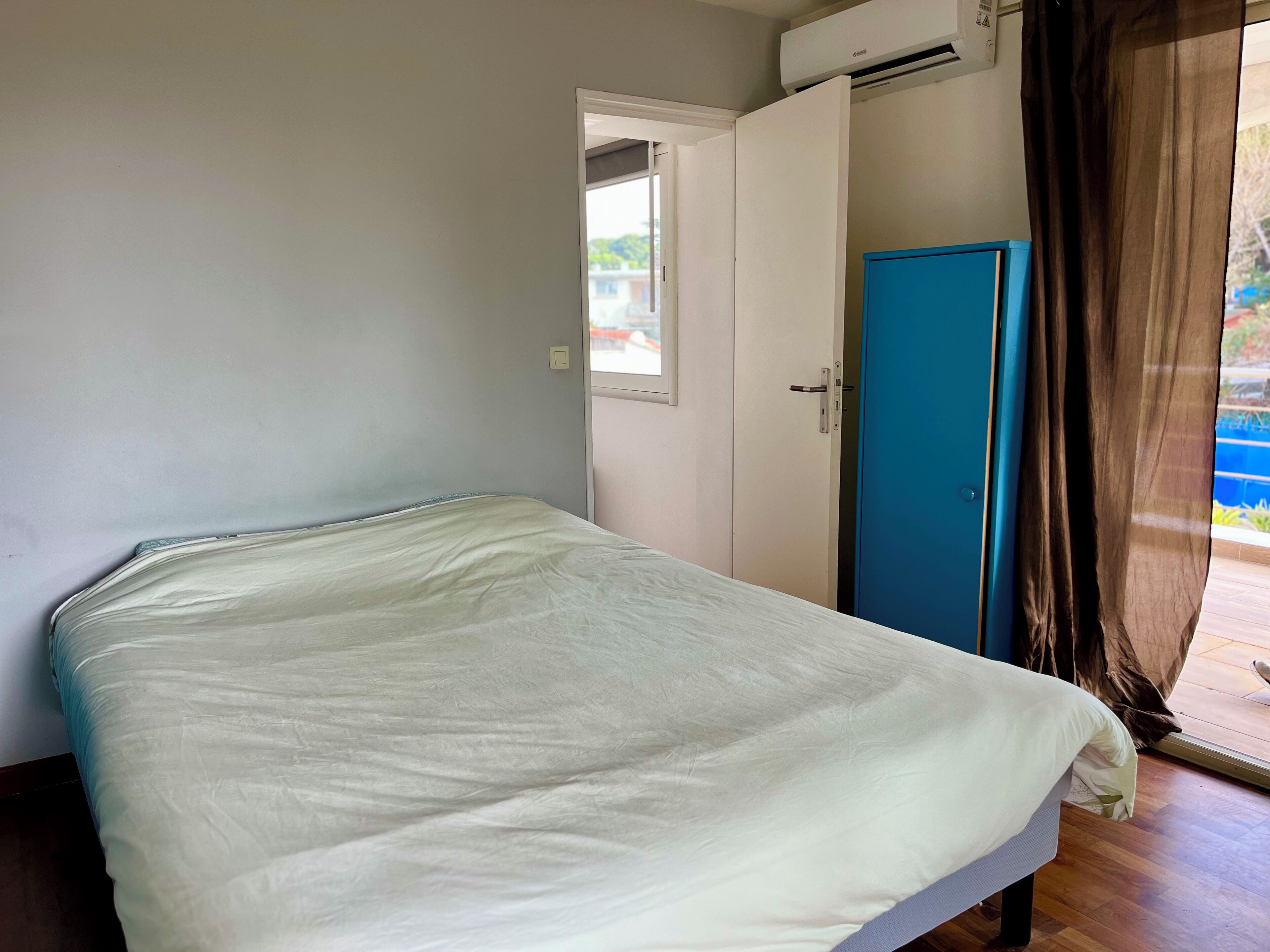 A room with a bed, a blue door, and an air conditioning unit.