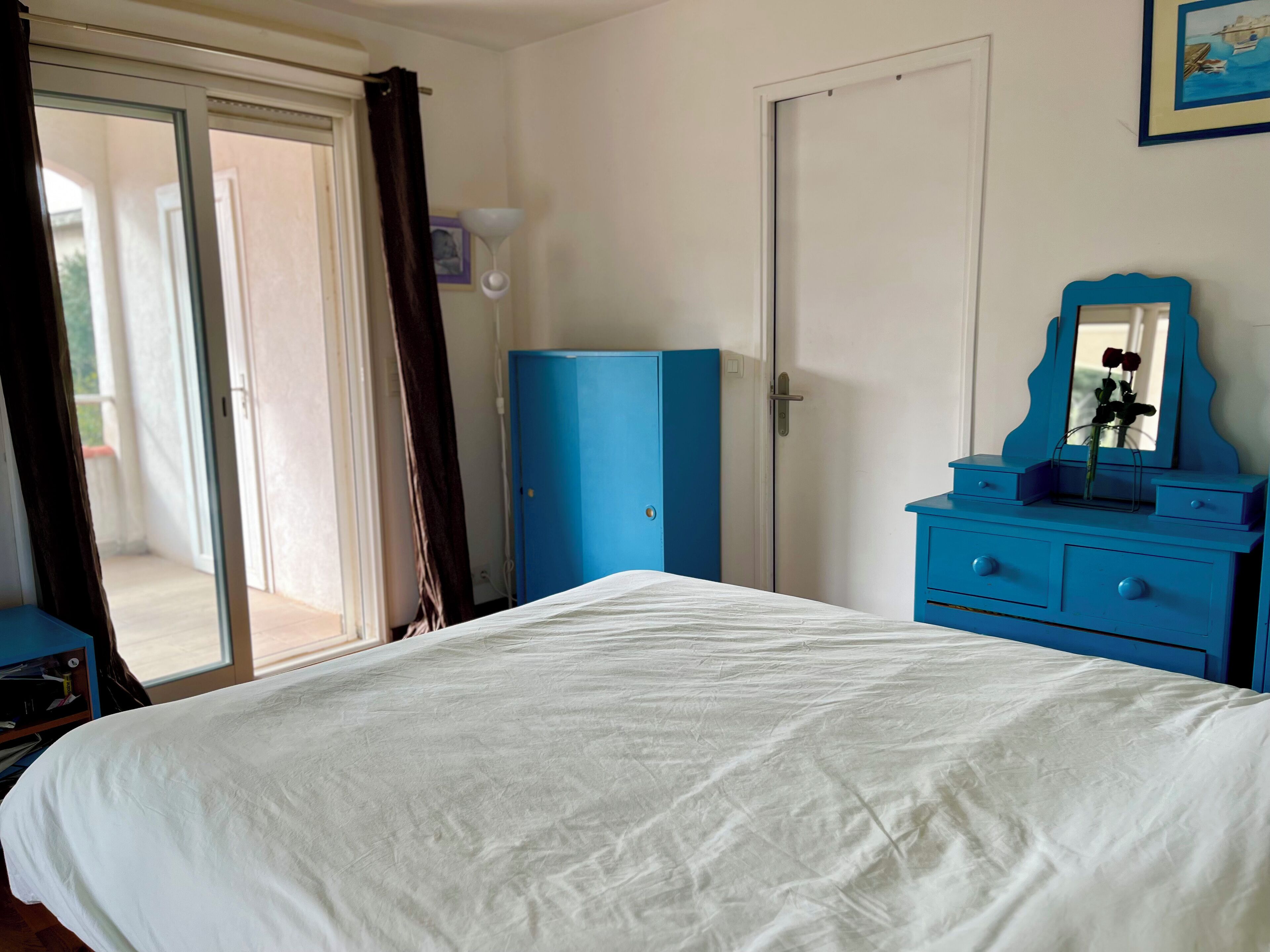 Un dormitorio con cama, un aparador azul, una puerta y una ventana con cortinas.