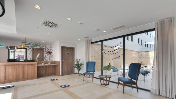 A modern hotel lobby with a reception desk, seating area, and large windows offering views of the building's interior. - Livensa Living Salamanca Parking Free (Salamanca)