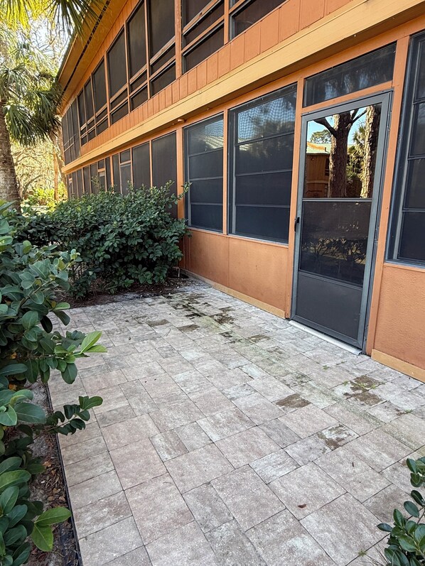 A building with large windows and a door, surrounded by a paved area with some greenery.