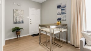 A modern dining area with a glass-top table and metal chairs, a white door, and a potted plant. - Camellia: Studio Apt, 4 Minute walk to A&M (College Station)