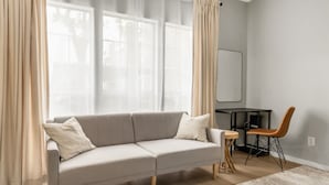 A modern living room with a grey sofa, a small wooden table, and a chair. - Camellia: Studio Apt, 4 Minute walk to A&M (College Station)
