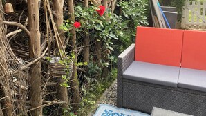 Un jardín con un sofá de mimbre, un tapete estampado y una cerca blanca de piquete.
