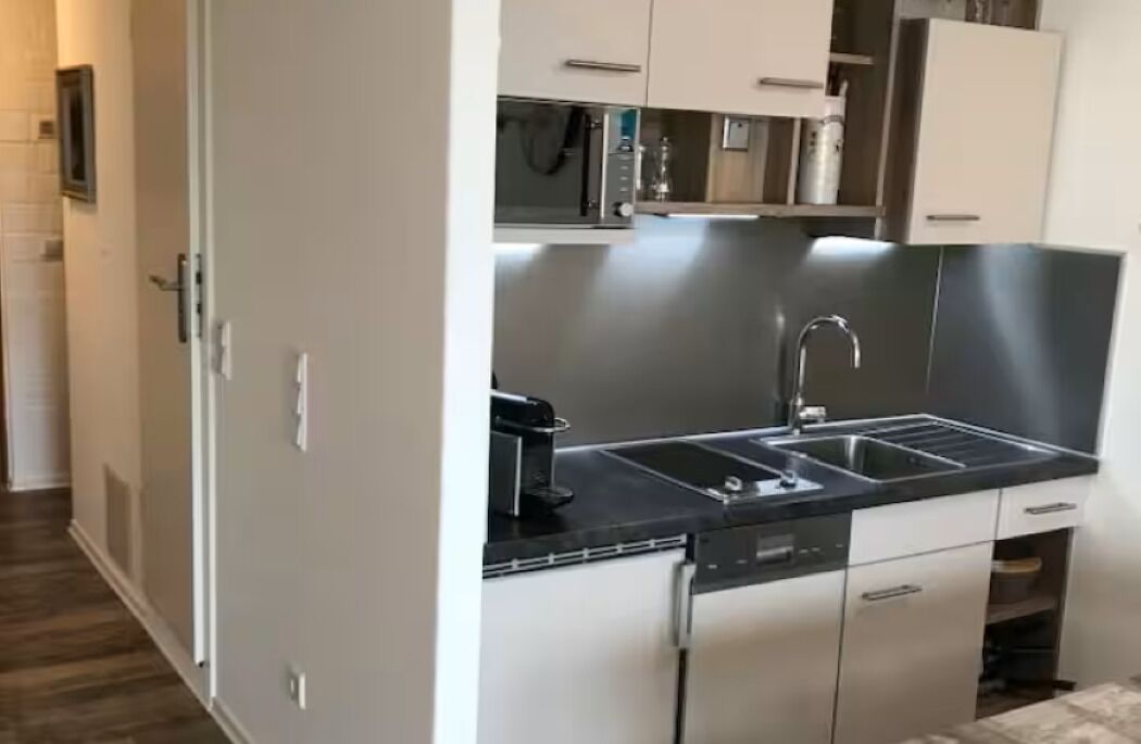 A compact kitchen with a black countertop, stainless steel appliances, and white cabinetry.