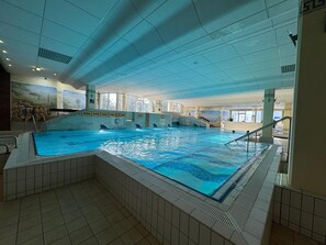 Una piscina coperta con diverse corsie, pareti piastrellate e un soffitto con illuminazione a incasso.