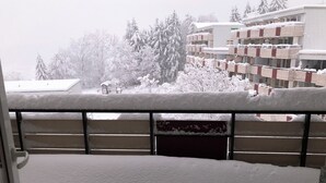 Un balcón con acumulación de nieve, con vista a un edificio de varios pisos y un estacionamiento.
