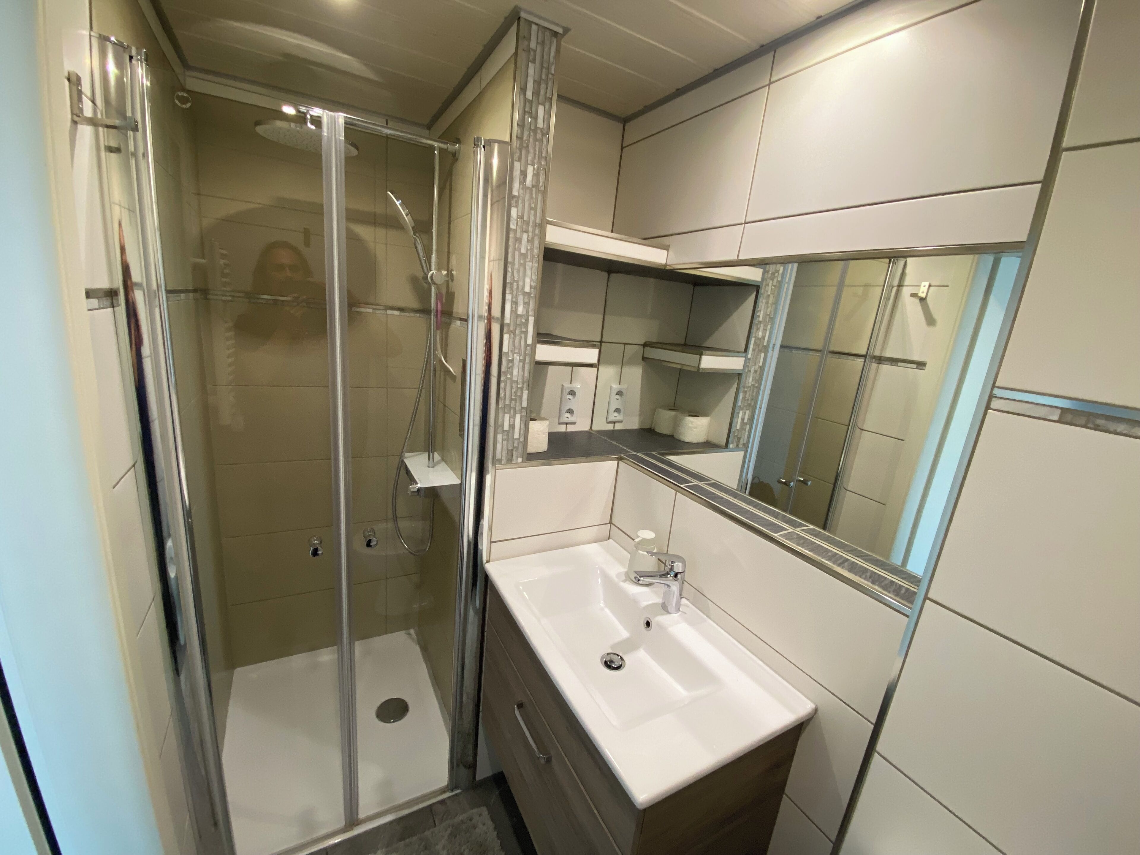 Une salle de bain moderne avec une douche à parois de verre, un lavabo blanc et un miroir au-dessus.