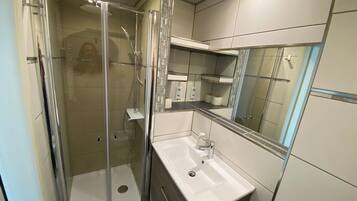 Une salle de bain moderne avec une douche à parois de verre, un lavabo blanc et un miroir au-dessus.