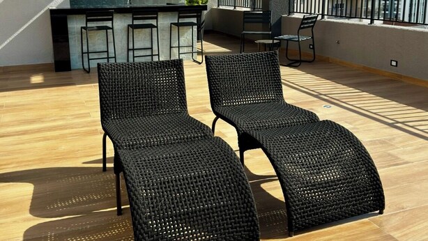 Une terrasse sur le toit, dotée de deux fauteuils de relaxation en osier noir, d’un coin bar avec un mur arrière en pierre et offrant une vue sur le panorama urbain.