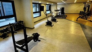 Une salle de sport équipée de divers appareils d’exercice, dotée de grandes fenêtres et offrant un espace généreux.