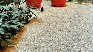 Un petit espace extérieur agrémenté de deux jardinières rouges, d’un chemin de gravier et de plantes vertes.