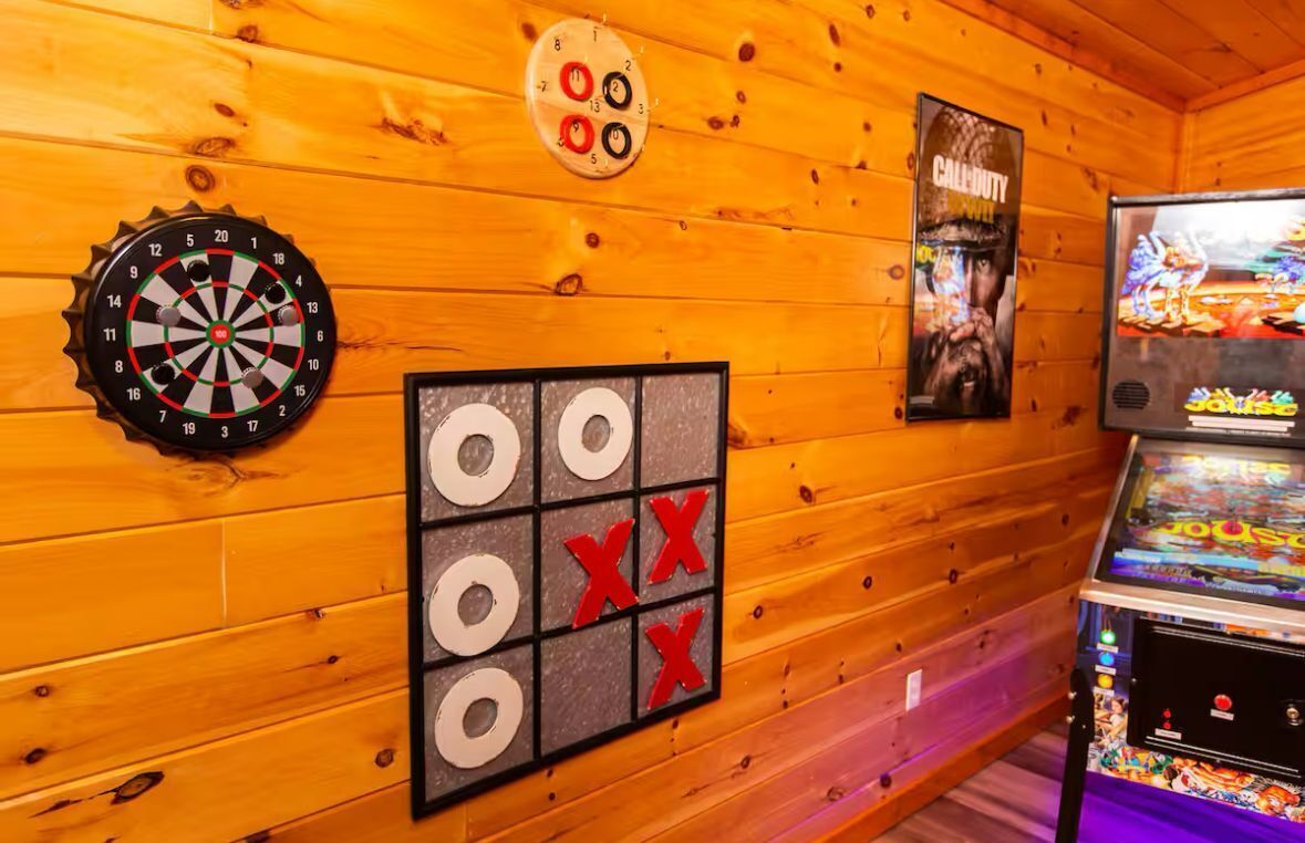 Een kamer met houten wanden, een dartbord, een tic-tac-toe spel, een poster van Call of Duty en een videogame apparaat.