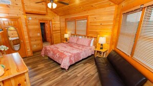 A wooden cabin bedroom with a bed, bedside lamps, a bench, and a mirror.