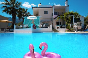 Una piscina con flamencos inflables, un edificio blanco con balcones y mobiliario exterior.