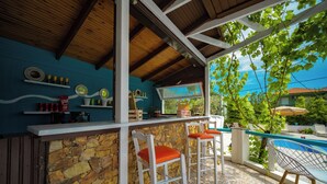 A covered outdoor bar area with stone walls, wooden ceiling, and a poolside view. - Aegli Hotel Studios (Thasos)