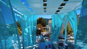 An outdoor patio with blue curtains, a table with a vase, and a sofa. - Aegli Hotel Studios (Thasos)