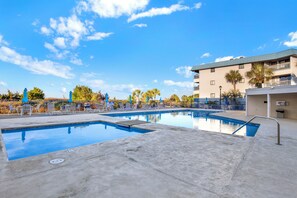 Une piscine dotée de plusieurs couloirs, de chaises longues et d’un bâtiment avec des balcons.
