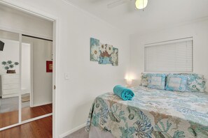 Une chambre à coucher comprenant un lit, une table de chevet, un téléviseur fixé au mur et une fenêtre avec des stores.