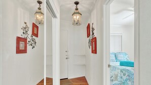 A hallway with a wooden floor, a white door, and a bed with a blue bedspread in the background. - Charming 1-bedroom condo in serene Tybee Island (Tybee Island)