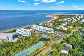 Vue aérienne d’un hôtel situé sur la côte, composé de plusieurs bâtiments, avec une plage et des courts de tennis.
