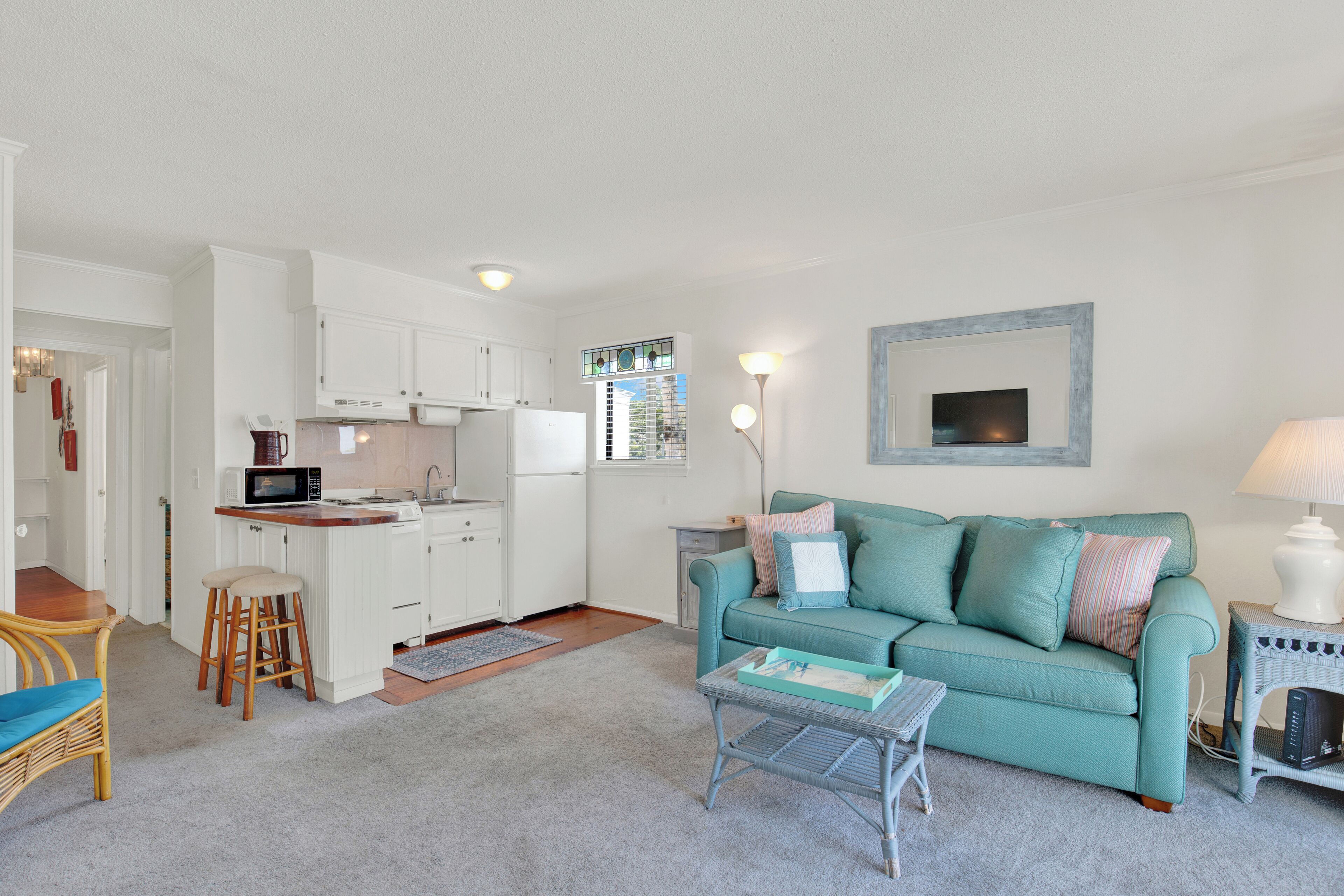 A compact living space with a kitchenette, a teal sofa, a small coffee table, and a wicker chair.