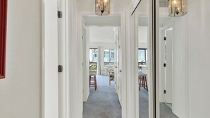 A hallway with white walls, wooden flooring, and a carpeted area leading to a dining space with chairs and a table. - Charming 1-bedroom condo in serene Tybee Island (Tybee Island)