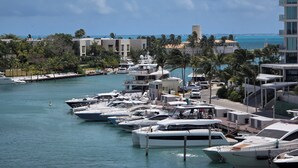 A marina with several yachts docked, surrounded by buildings and palm trees. - Marea Puerto Cancun, luxury+comfort+the best view (Cancún)