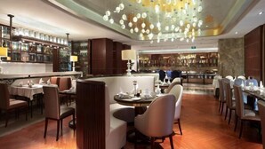 A restaurant with round tables, cushioned seating, and a bar area with shelves of bottles.