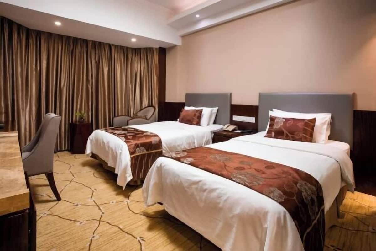 Habitación de hotel con dos camas, un escritorio, una silla y una cortina.