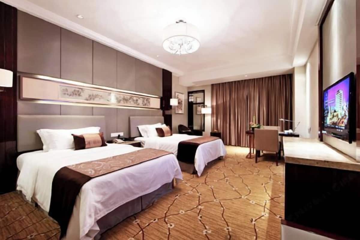 Habitación de hotel con dos camas, televisión, escritorio y un ventanal grande con cortinas.