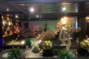 A lobby with a modern design, featuring a central sculpture, potted plants, and ambient lighting. - Haiyan Hotel (Haiyan)