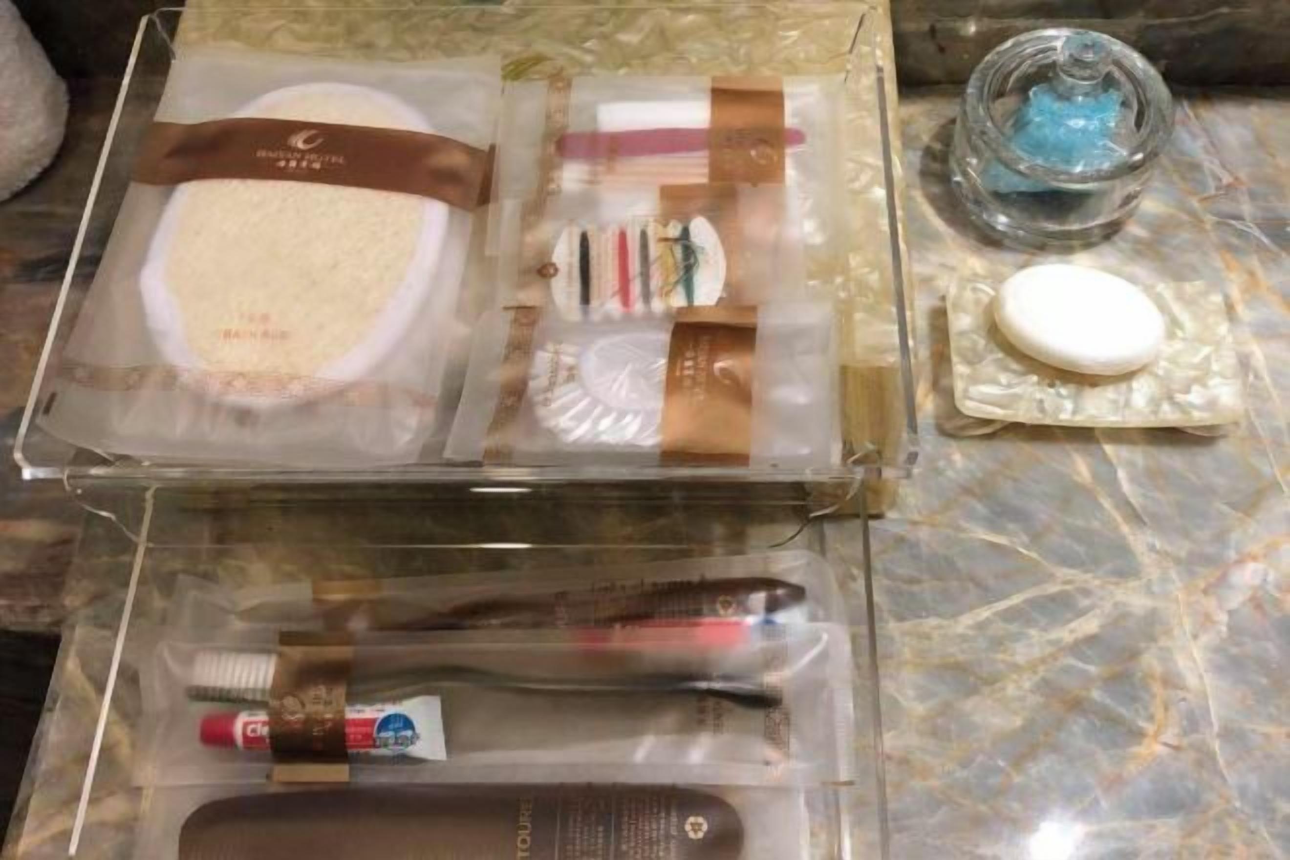 A set of toiletries and a small container of blue liquid, likely shampoo, on a marble surface.