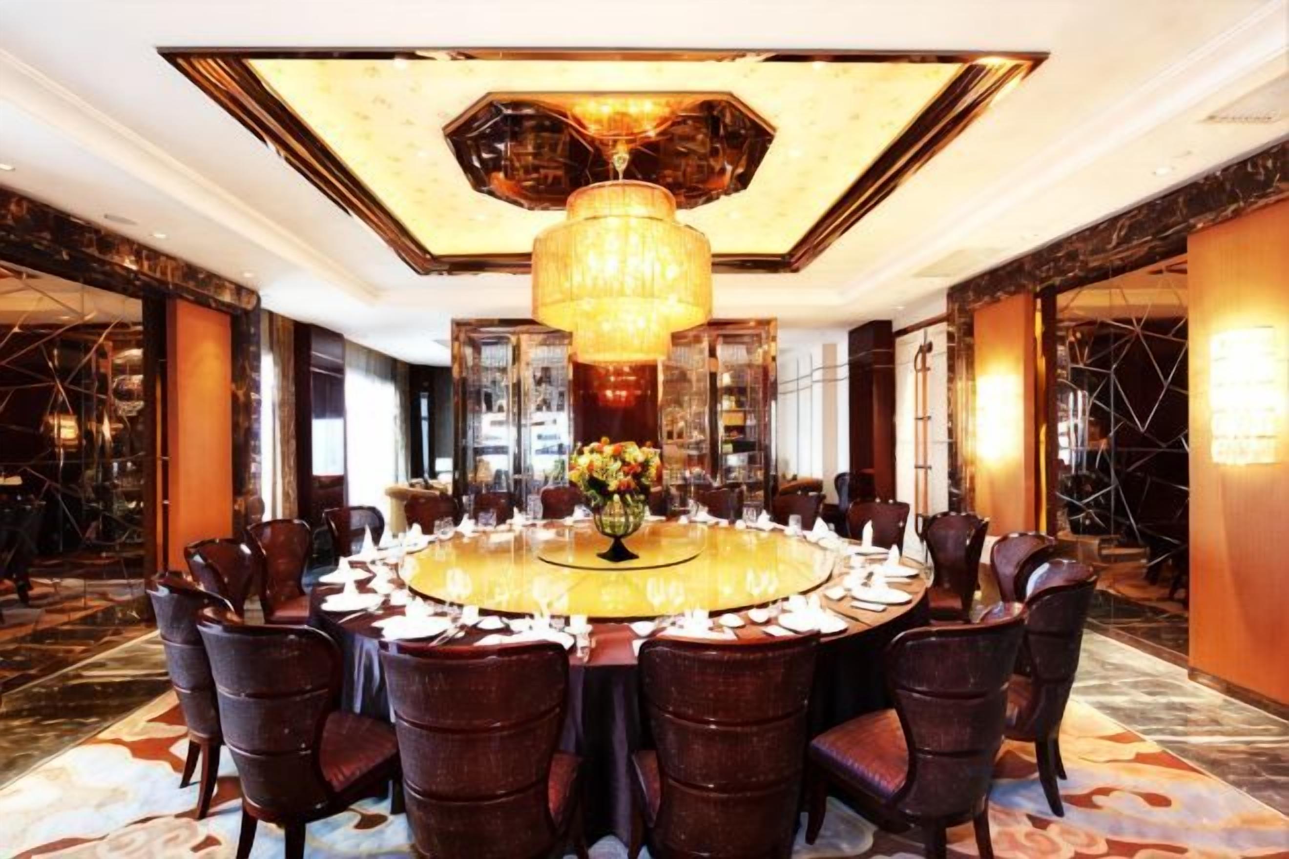 A round table with chairs, a chandelier, and a floral centerpiece in a hotel room.