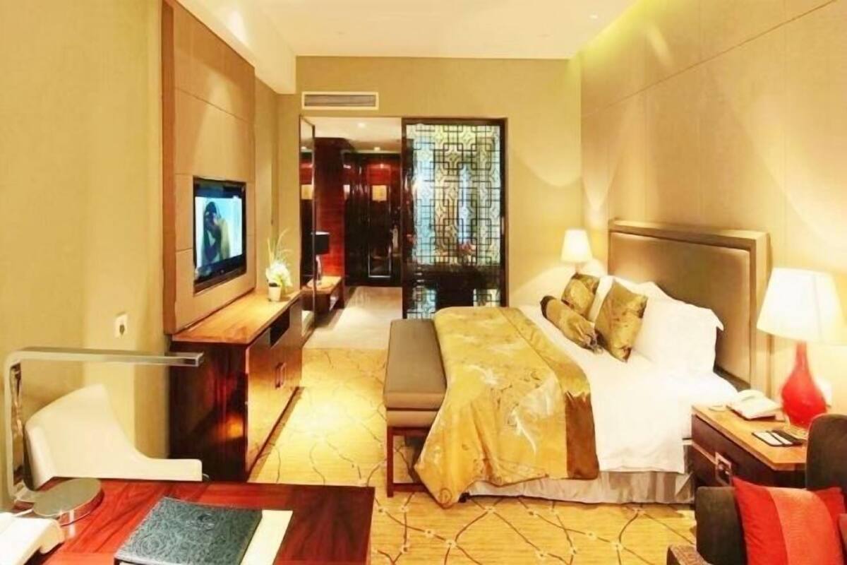 Habitación de hotel con cama, mesita de noche, televisor y una zona de estar con una silla y una mesa.