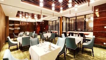A hotel dining area with tables set for service, a patterned carpet, and a modern ceiling design.