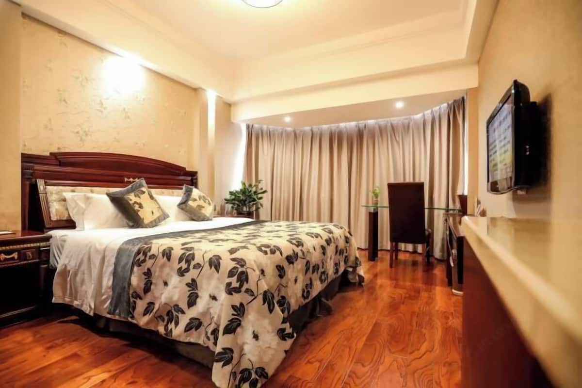 Una habitación de hotel con una cama grande, cabecero de madera y televisor montado en la pared.