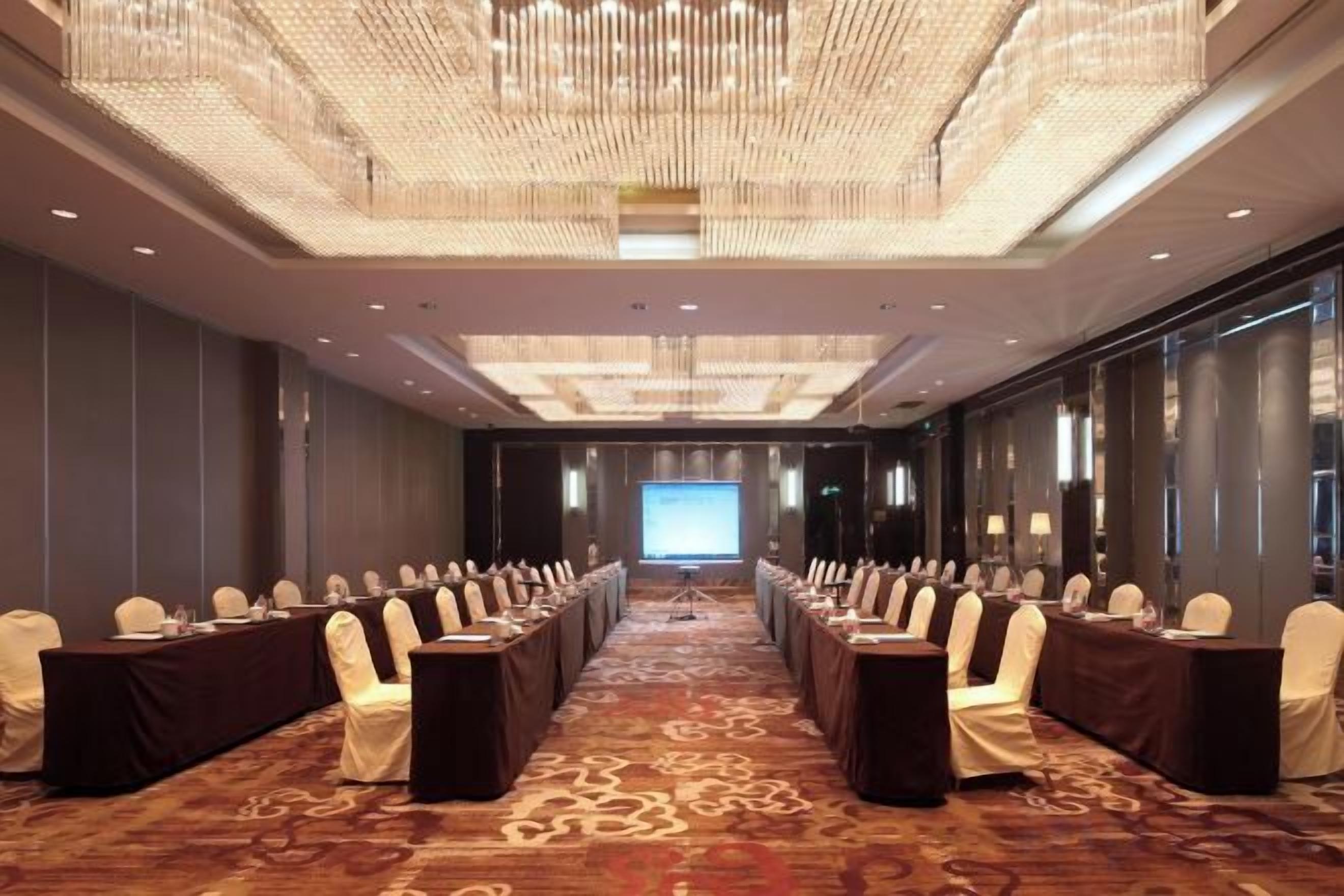 A conference room with a long table, chairs, and a large screen at the front.