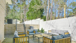 Un patio exterior con pared de ladrillo, cerca blanca y terraza de madera.