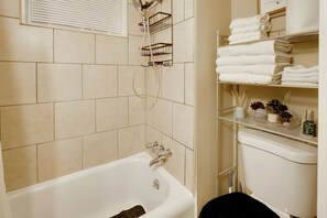 A bathroom with a bathtub, a shower, and a toilet. There are shelves with towels and toiletries. - 1 Mi to Dtwn Wilmington: Convenient + Cozy Home! (Wilmington)