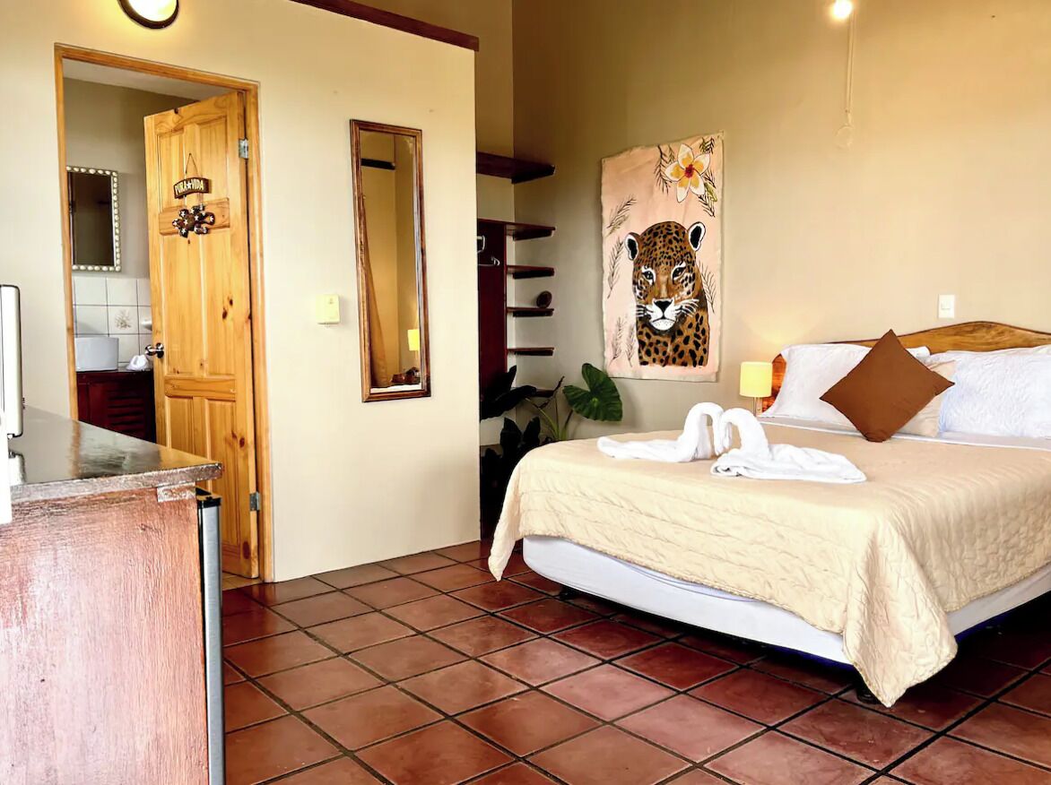 A hotel room with a bed, a wooden door, a mirror, and a painting of a leopard.