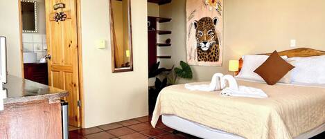 A hotel room with a bed, a wooden door, a mirror, and a painting of a leopard.