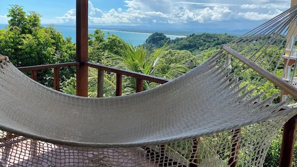 A hammock on a wooden deck overlooking a lush landscape with a view of the sea. - Mi Zaru Sea View Animal Paradise (Quepos)
