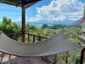 Una hamaca sobre una terraza de madera con vistas a un paisaje exuberante y al mar.